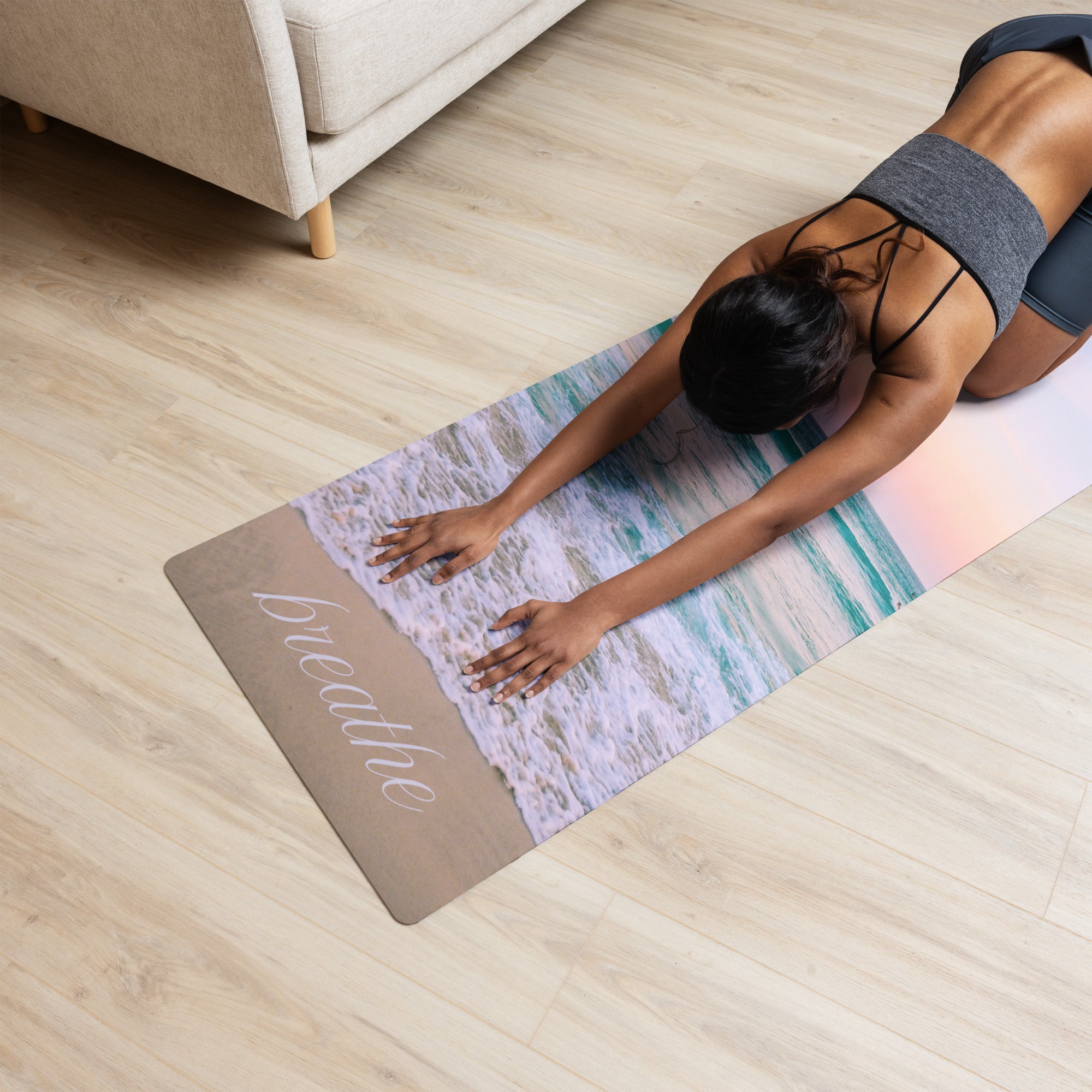 A person is doing yoga on a mat with a beach and ocean design, including the word 'BREATHE' on the mat.