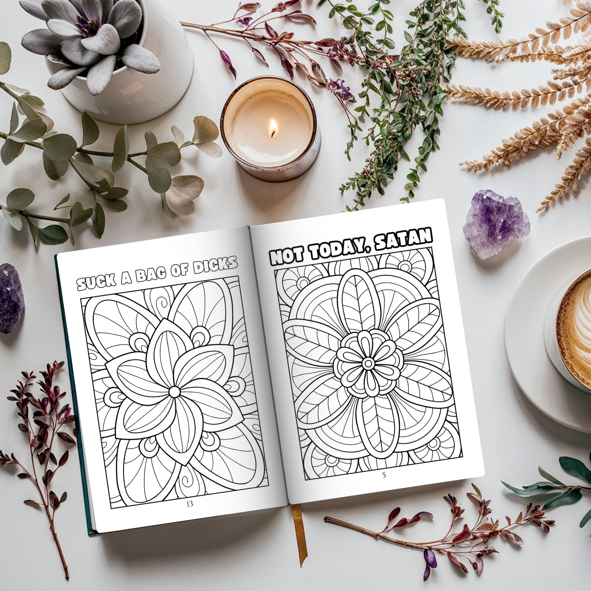 Coloring book open to pages with floral designs and humorous text, surrounded by candles, plants, and a cup of coffee on a white surface.